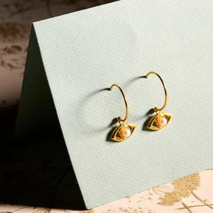 Gold earrings with pearl accents on a textured green card