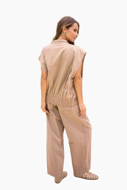 Woman wearing a beige sleeveless top and pants on a white background