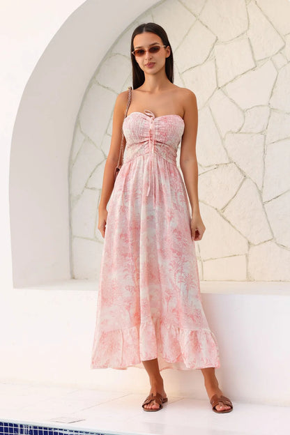 Woman wearing a pink floral dress standing against a white stone wall.