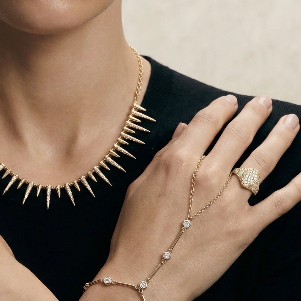 Gold spiked necklace, bracelet, and ring on a person against a neutral background