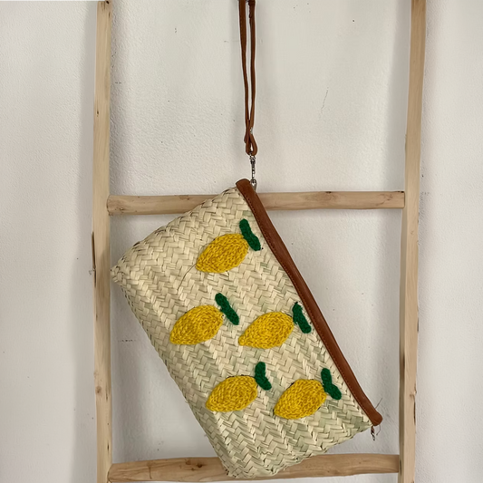 Woven clutch bag with pineapple patterns hanging on a wooden ladder against a white wall.