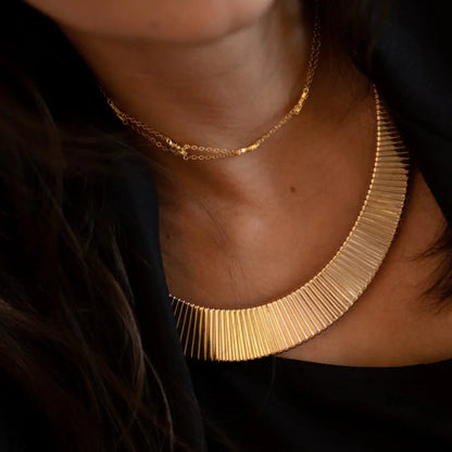 Close-up of a person wearing a gold necklace with a textured design.
