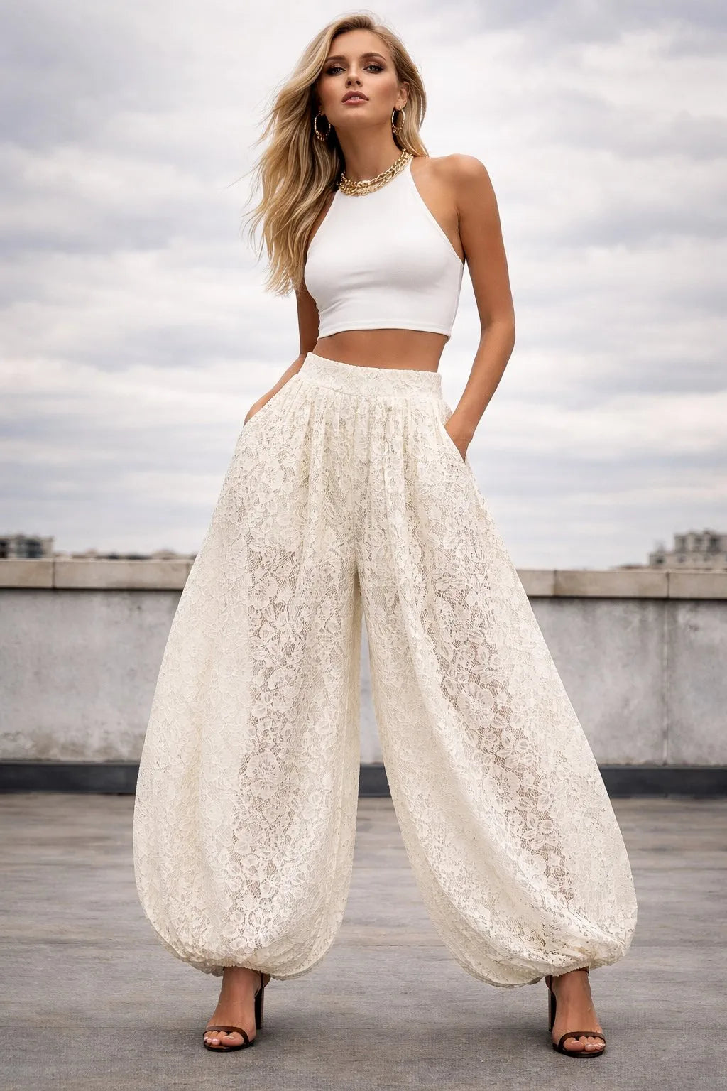 Woman wearing a white sleeveless top and wide-leg pants on a rooftop with a cloudy sky.