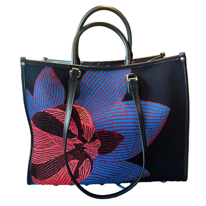 Black handbag with red and blue floral embroidery on a glass surface.