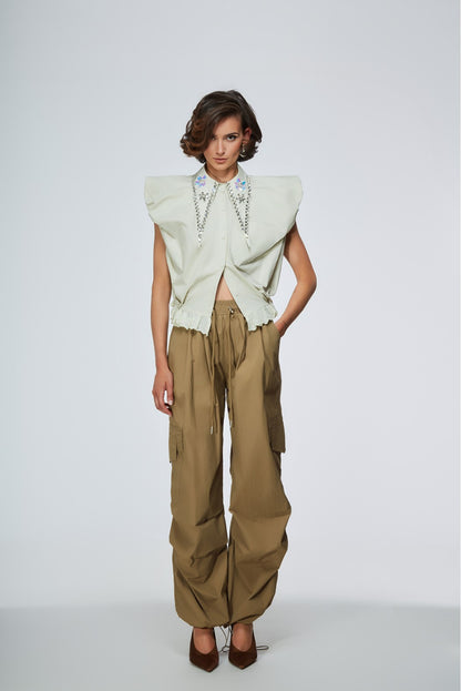 Woman wearing a light green top with floral details and beige pants on a white background