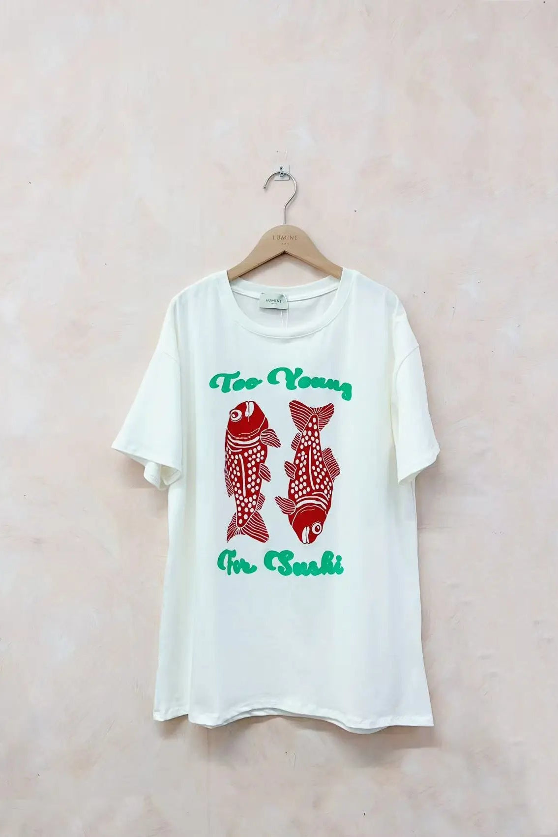 White t-shirt with red fish graphic and text on a light pink background