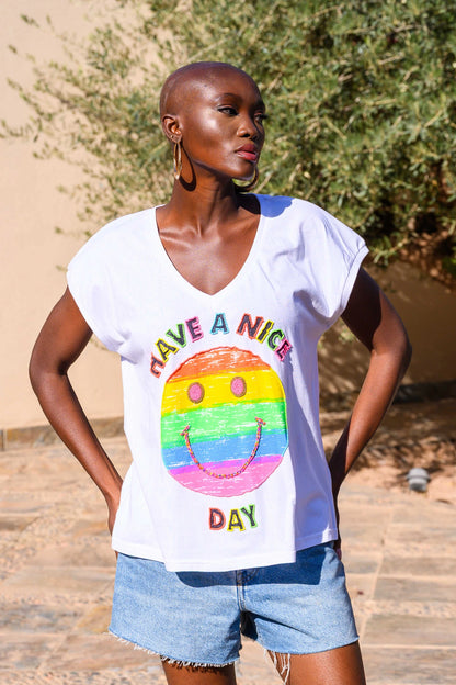 Woman wearing a white t-shirt with a colorful smiley face design and text outdoors.