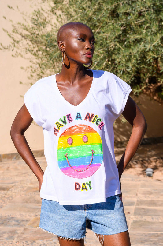 Woman wearing a white t-shirt with a colorful smiley face design and text outdoors.
