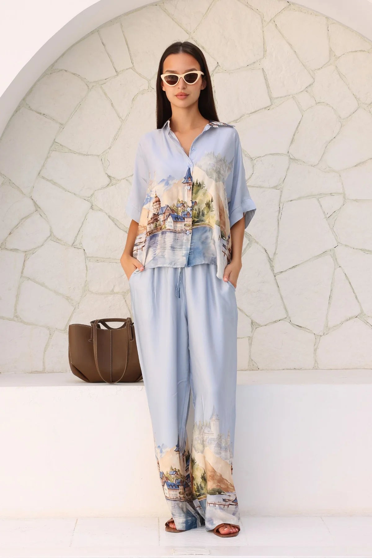 Woman wearing a matching outfit with a light blue shirt and pants against a stone wall.