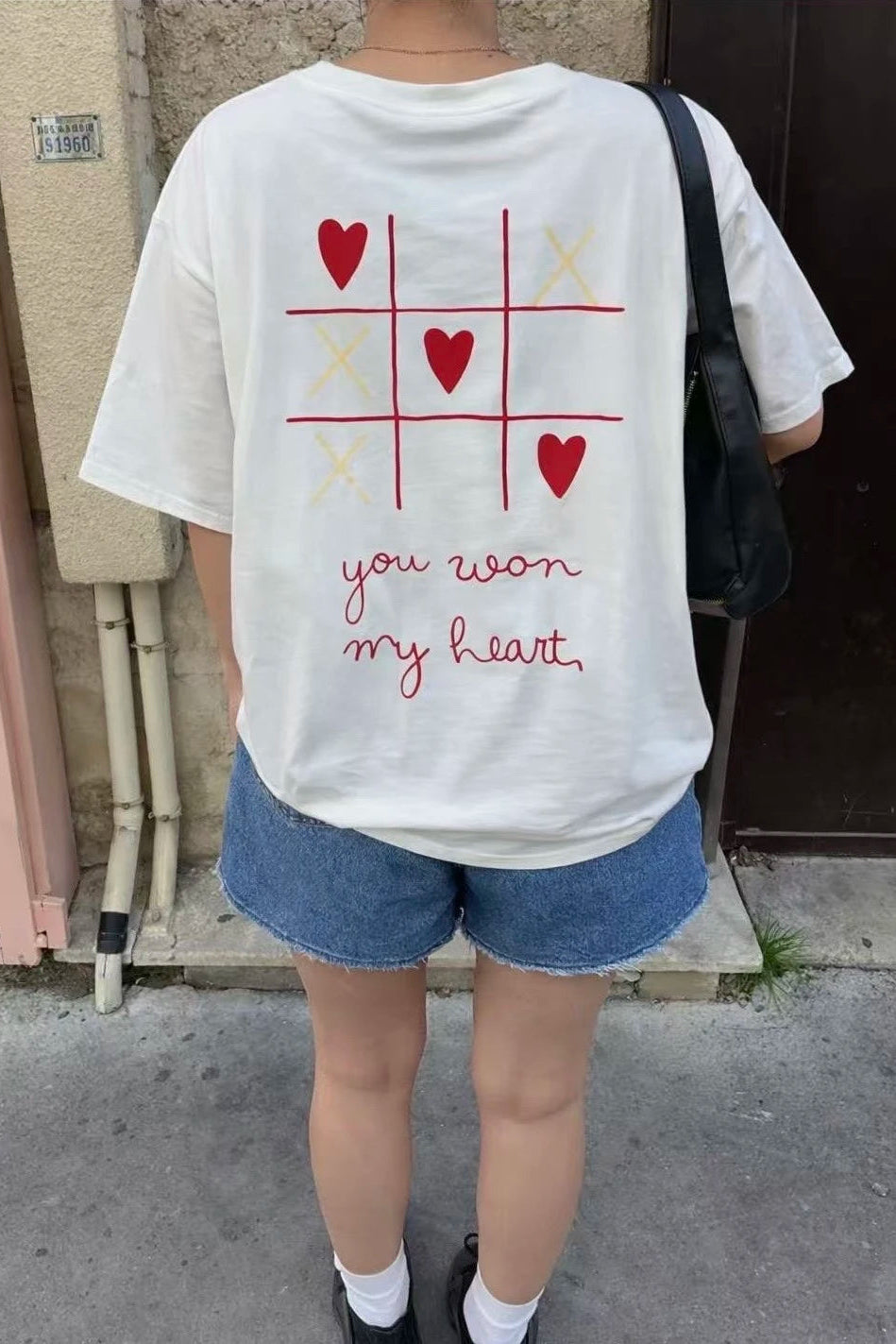 Person wearing a white t-shirt with a graphic design and text, standing outdoors.