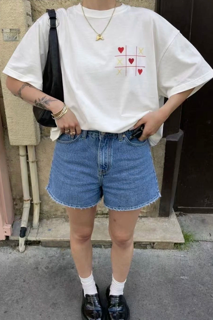 Person wearing a white t-shirt with a design and blue shorts outdoors.