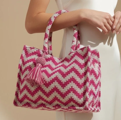 Pink and white zigzag patterned bag with a tassel held by a person against a beige background