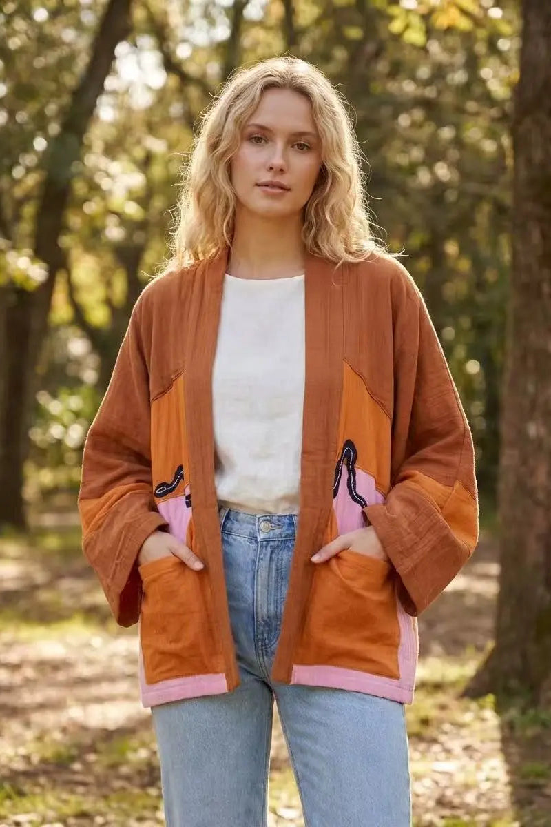 Woman wearing a brown jacket with pink accents in a forest setting